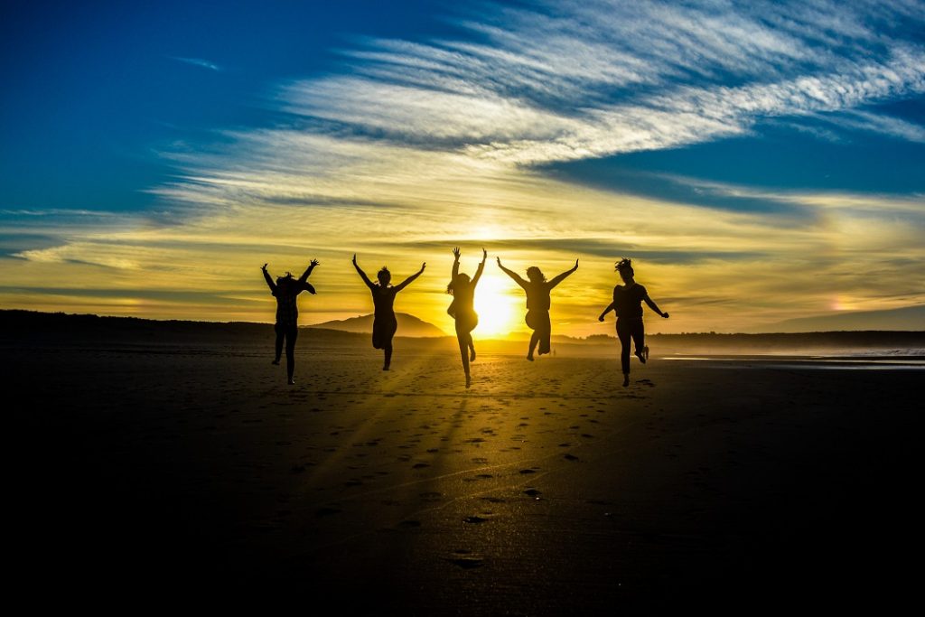 Beautiful Sunset With People Silhouettes Jumping hands outstretched.