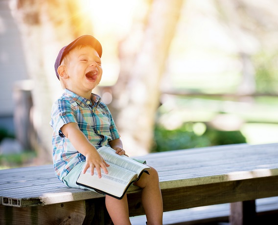 Kid on bench laughing reading a book